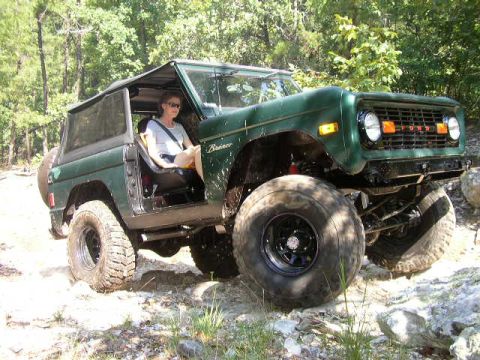 1995 Ford Bronco - This classic Ford Bronco is navigating a rough, wooded terrain with large tires.