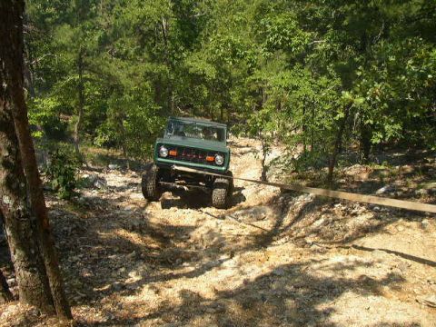 1995 Ford Bronco - A green 1978 Ford Bronco navigates a challenging off-road path in a wooded area.