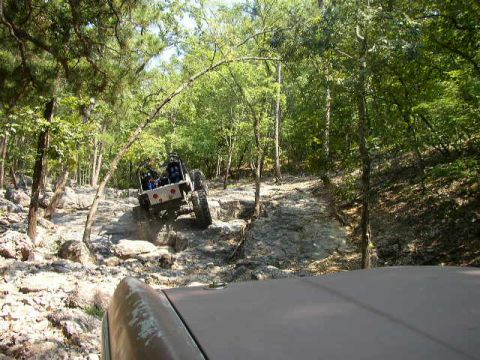 1995 Ford Bronco - A Jeep navigates a challenging, rocky off-road path through a wooded area.