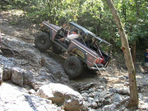 1995 Ford Bronco - A modified Ford Bronco navigates a challenging rocky incline in a wooded area.