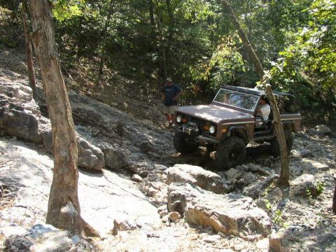 1995 Ford Bronco - A brown Ford Bronco navigates a challenging rocky incline, demonstrating its off-road capabilities.