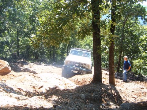 1988 Ford Bronco - White Ford Bronco tackles an off-road trail with a person watching nearby.