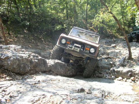 1995 Ford Bronco - A brown Ford Bronco tackles a challenging rocky trail with another vehicle visible in the background.