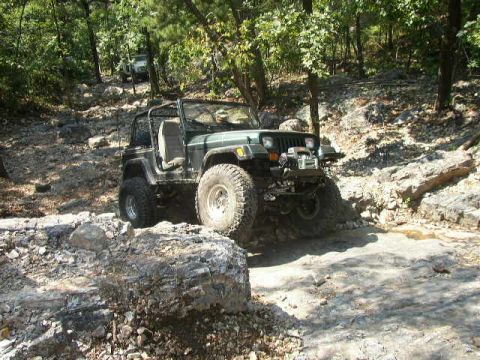 1995 Ford Bronco - A green Jeep Wrangler navigates a challenging rocky terrain with another vehicle visible in the background.