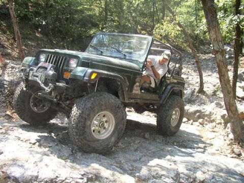 1995 Ford Bronco - A green Jeep Wrangler tackles a challenging rocky path, demonstrating its off-road capabilities.