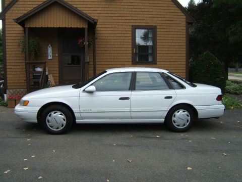 1998 Ford Taurus - Side view of a white 1998 Ford Taurus sedan parked in front of a house.