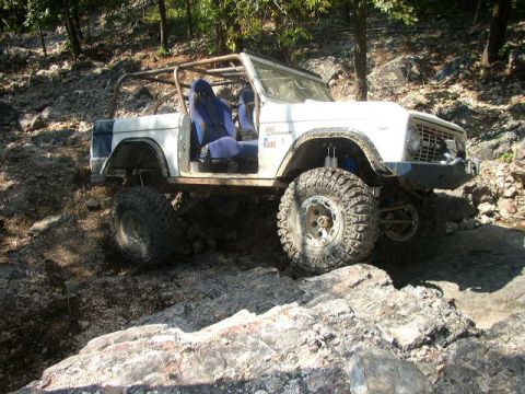 1995 Ford Bronco - This modified off-road vehicle navigates a rocky, wooded terrain.