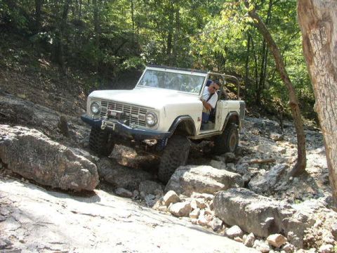 1995 Ford Bronco - A white 1978 Ford Bronco tackles a challenging off-road course, demonstrating its capability on rough terrain.