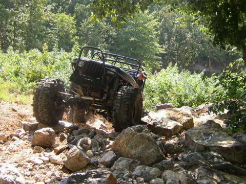 1995 Ford Bronco - A modified off-road vehicle navigates a rocky terrain on a sunny day.