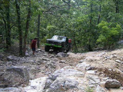 1995 Ford Bronco - A black 1995 Ford Bronco navigates a challenging rocky path through a wooded area.