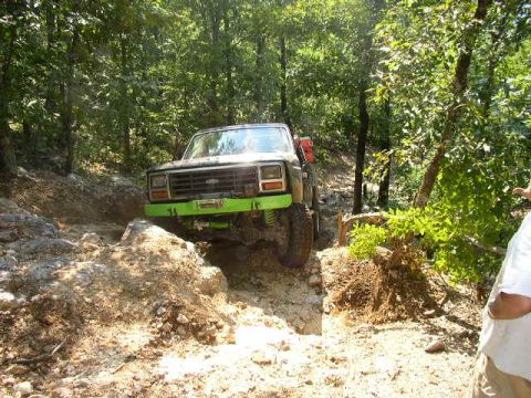 1995 Ford Bronco - Vehicle is navigating a challenging rocky trail in a dense forest environment.