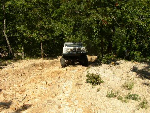 1995 Ford Bronco - A white SUV navigates a rocky, off-road trail surrounded by dense foliage.