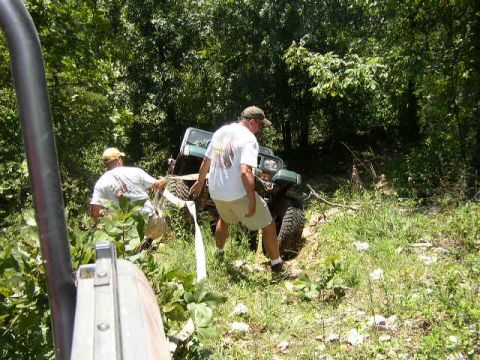 1995 Ford Bronco - Two men assist a green off-road vehicle stuck in a ditch, using a strap to pull it free.