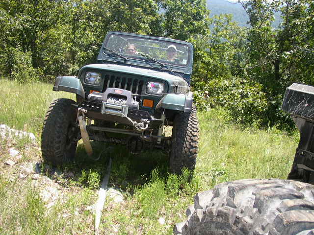 Green Jeep Wrangler with winch on a grassy trail, another vehicle's tire in foreground