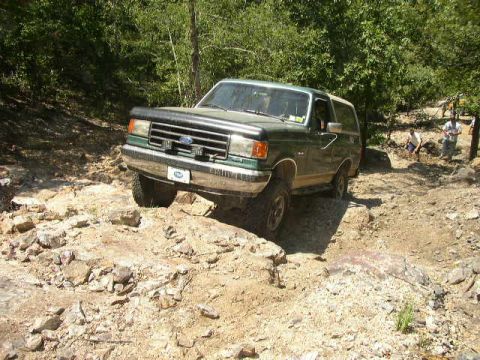 1995 Ford Bronco - A green Ford Bronco tackles a challenging rocky terrain on an off-road trail.