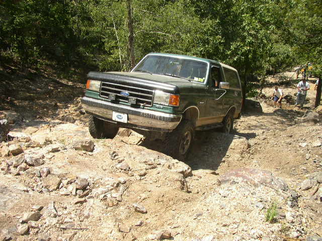 Green Ford Bronco with a black bug deflector on the hood navigates a rocky off-road trail