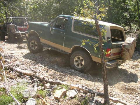 1995 Ford Bronco - A green 1995 Ford Bronco navigates a rocky off-road trail, with another vehicle visible behind it.