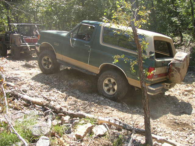 Green 1995 Ford Bronco with tan top and spare tire on rear, driving off-road