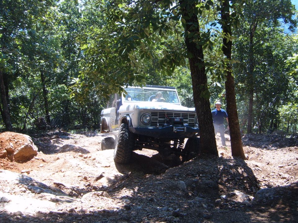 White Ford Bronco with large tires on rocky trail, driver visible