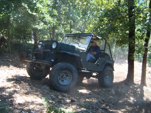 1988 Ford Bronco - A man drives a green Jeep CJ-5 off-road on a sunny day.