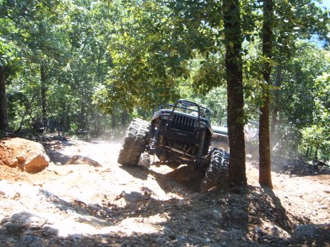 1988 Ford Bronco - An off-road vehicle navigates a challenging, wooded trail with another vehicle visible behind it.