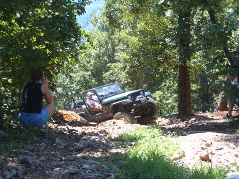 1988 Ford Bronco - Off-roading Jeep Wrangler navigates a challenging dirt trail with spectators.