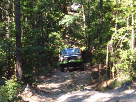 1988 Ford Bronco - This off-road SUV navigates a wooded trail, with another vehicle seen further up the incline.