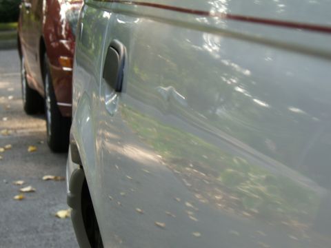 1998 Ford Taurus - A close-up shot shows the side of a silver car parked next to a maroon vehicle on a tree-lined street.
