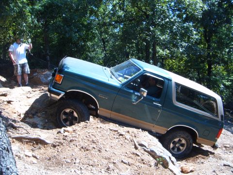 1988 Ford Bronco - A green Ford Bronco navigates a challenging off-road trail with a person watching.
