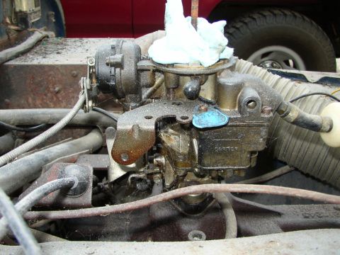 1973 Jeep CJ5 - Close-up of a Carter carburetor on an engine, with a red vehicle and tire visible in the background.