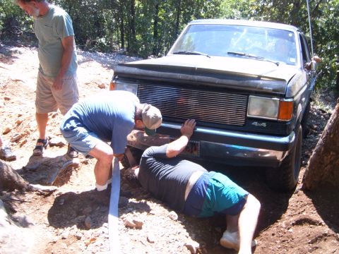 1988 Ford Bronco - A group of men attempt to free a stuck Ford truck from a ditch on a wooded trail.