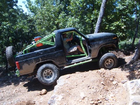 1988 Ford Bronco - Modified black Ford Bronco with a green roll cage navigates a rocky off-road trail.