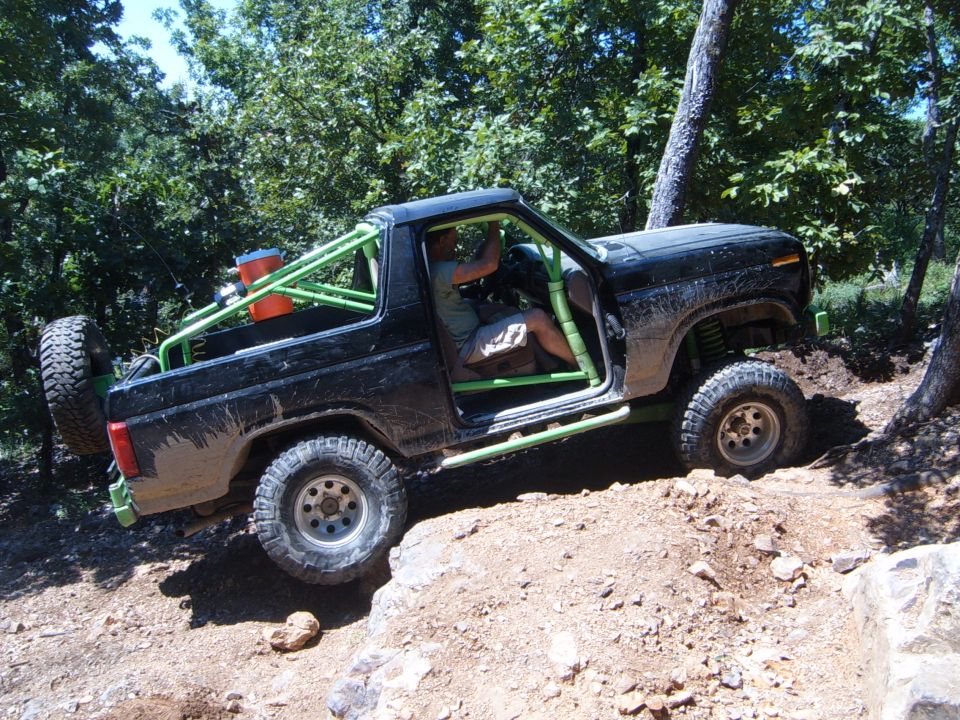 Black Ford Bronco with green roll cage and external spare tire driving off-road