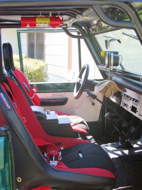 1985 Ford Bronco - The interior of a green SUV is shown, racing seats, a roll cage, and a mounted fire extinguisher.