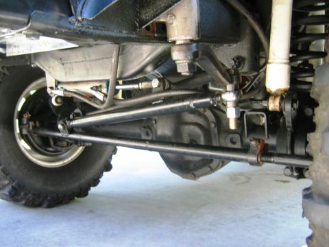 1985 Ford Bronco - Close-up view of the front axle and steering components of a vehicle, showing the suspension and linkage system.