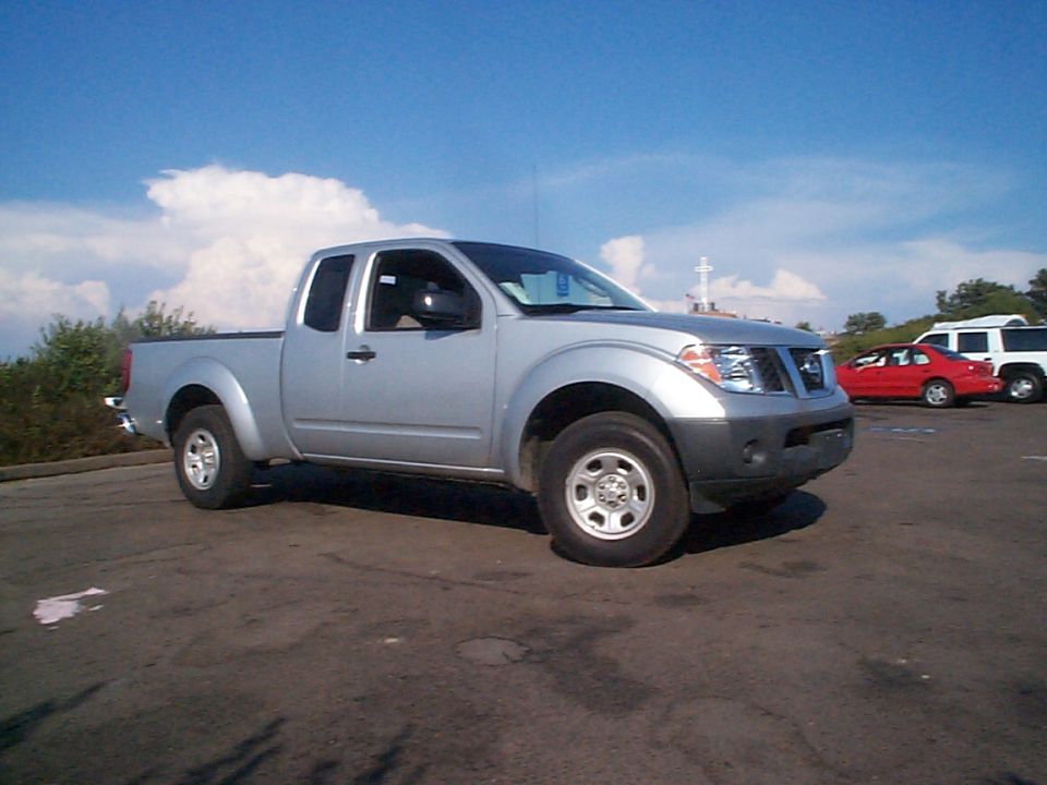 Silver 2005 Nissan Frontier pickup truck, driver's side front 3/4 view, parked on asphalt under a blue sky with clouds