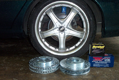 1995 Ford Taurus - New brake rotors and pads are laid out next to a car's aftermarket wheel and tire.