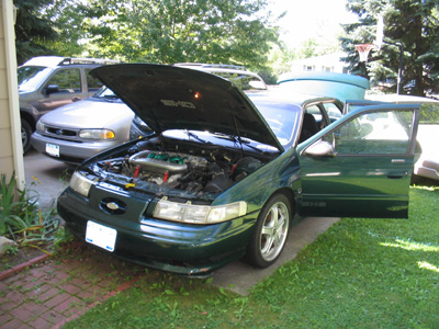 1995 Ford Taurus - A green 1995 Ford Taurus is shown with its hood and driver's door open, parked outside on a sunny day.