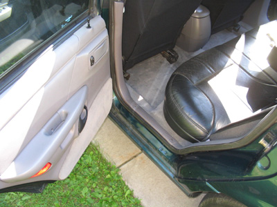 1995 Ford Taurus - The interior of a green car is visible through the open driver's side door, showing the back seat and door panel.