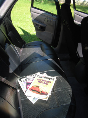 1995 Ford Taurus - Magazines are piled on the back seat of a car, one is a Car and Driver issue about a Taurus wagon.