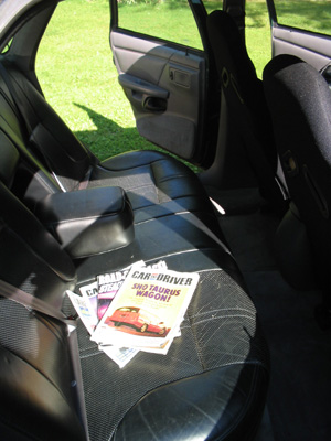 1995 Ford Taurus - Magazines are placed on the leather seats inside a car, with the door open to a grassy exterior.