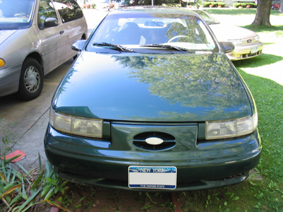 1995 Ford Taurus - A green sedan is parked in a driveway with two other vehicles visible.