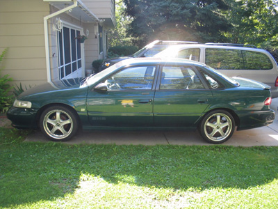1995 Ford Taurus - Side view of a green 1995 Ford Taurus sedan parked in front of a house.