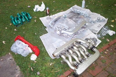 1995 Ford Taurus - Engine intake manifold parts, including silver and green painted components, laid out on grass.