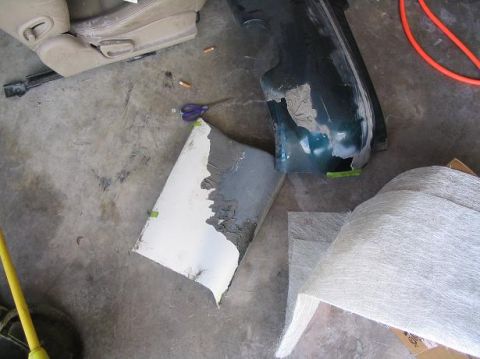 1994 Ford Probe - Car parts, including a seat and a damaged bumper, are laid out on a concrete floor with fiberglass matting.