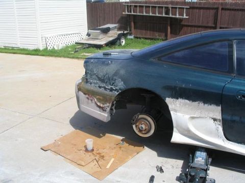 1994 Ford Probe - A car is being repaired, with body filler applied to the rear quarter panel and bumper, and the rear wheel removed.