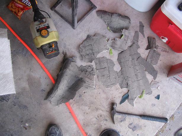Debris from a project, a weed trimmer, hammer, and a cooler on a concrete floor