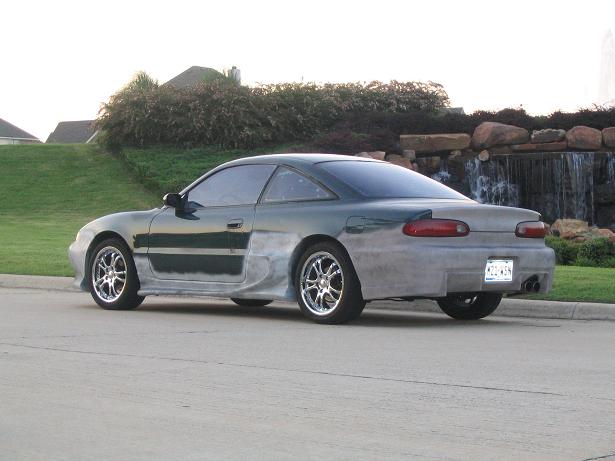 Green 1994 Ford Probe with unfinished bodywork, chrome wheels, and a rear spoiler, viewed from the rear three-quarter angle