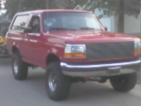 1989 Ford Bronco - Three-quarter front view of a lifted red two-door Ford Bronco parked on a driveway, showing fresh red paint on the hood and fenders with a…