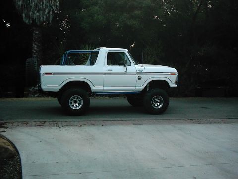 1978 Ford Bronco - A lifted 1978 Ford Bronco with a blue roll cage is parked on a street, seen from its side profile.